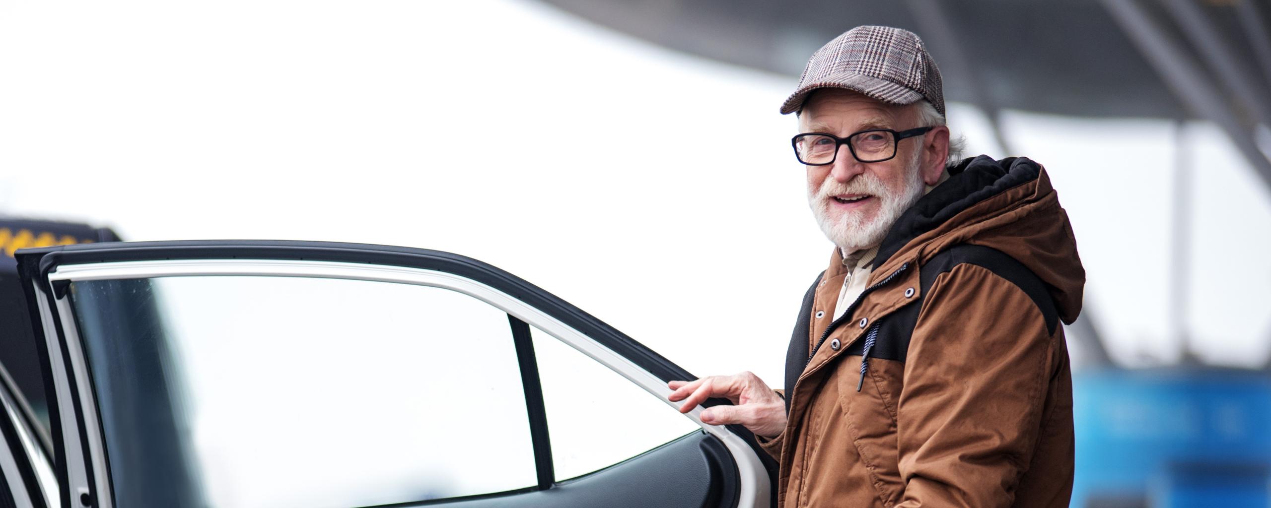 Oudere man met wandelstok bij portier van een taxi