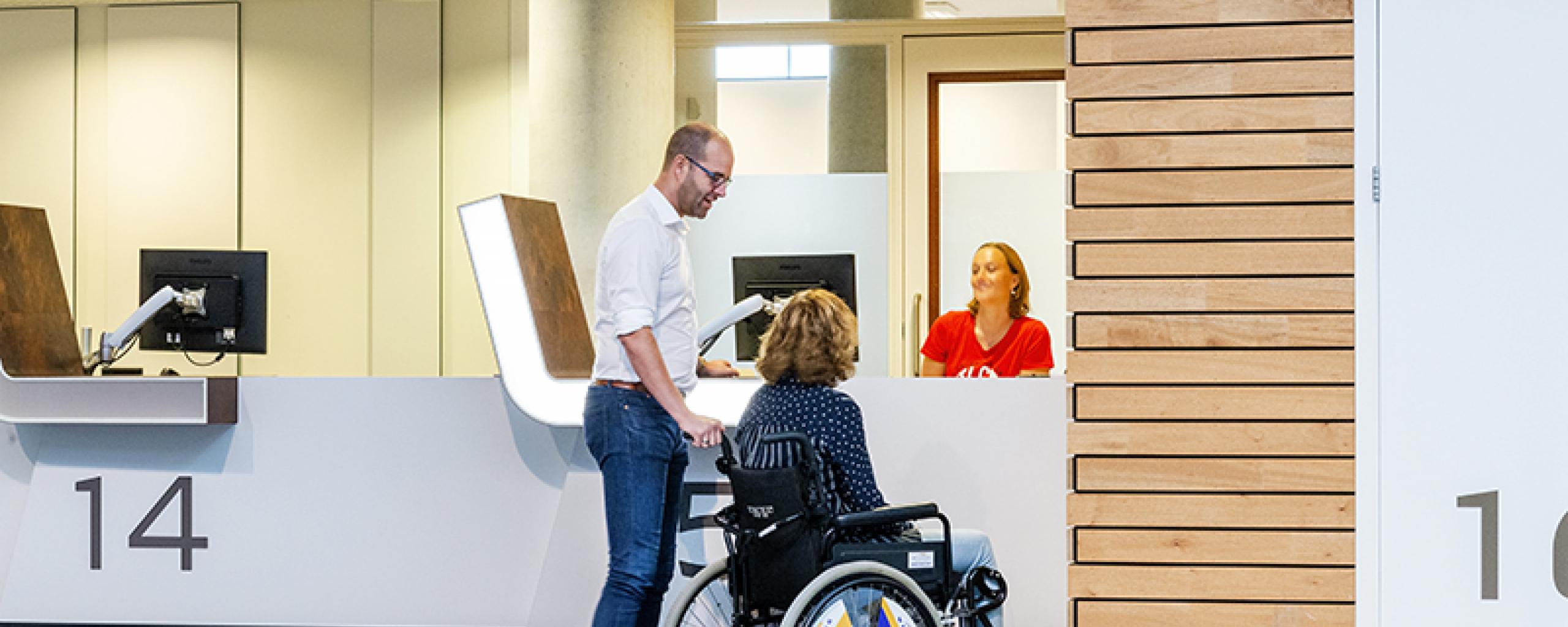 man met vrouw in rolstoel aan de balie van Team WijZ