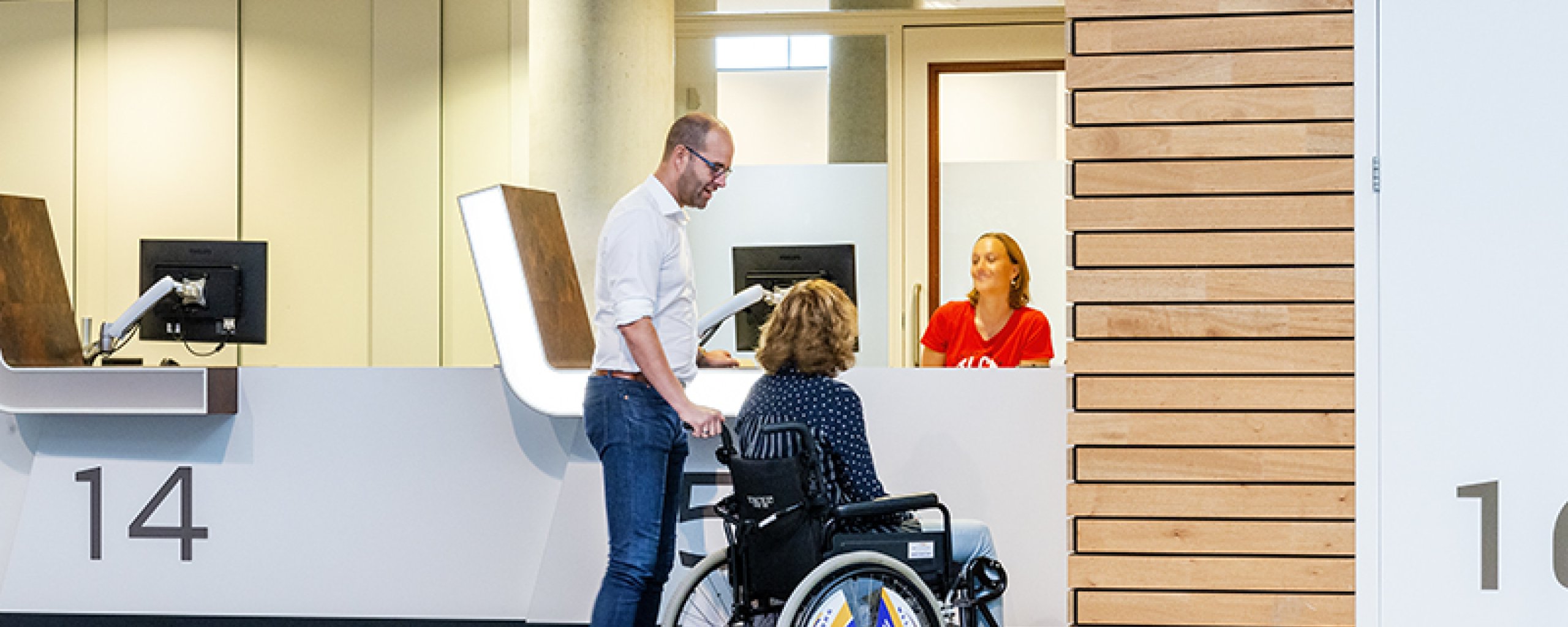 Balie Team WijZ met twee bezoekers, waarvan vrouw in rolstoel